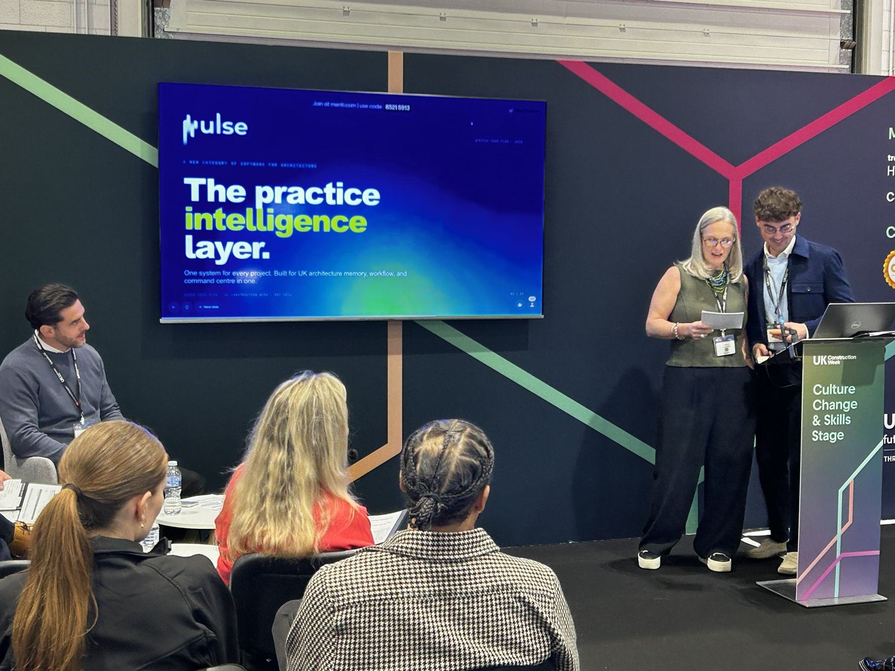 Lindsay and Lewis on stage beside the Pulse title slide